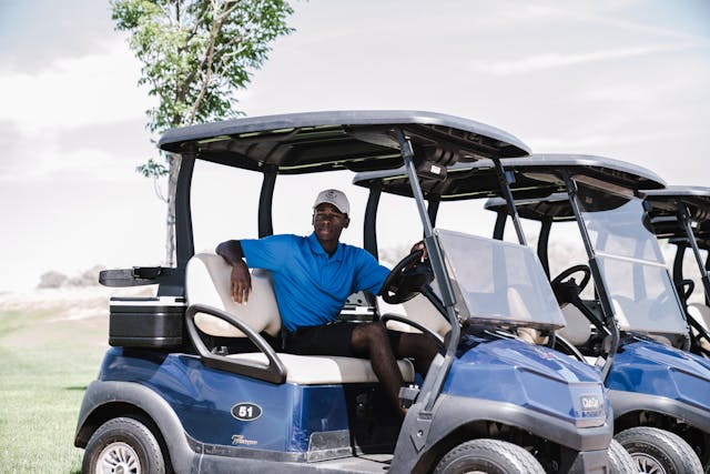 Golfer sitting in a blue Club Car golf cart on a golf course with premium design and canopy roof