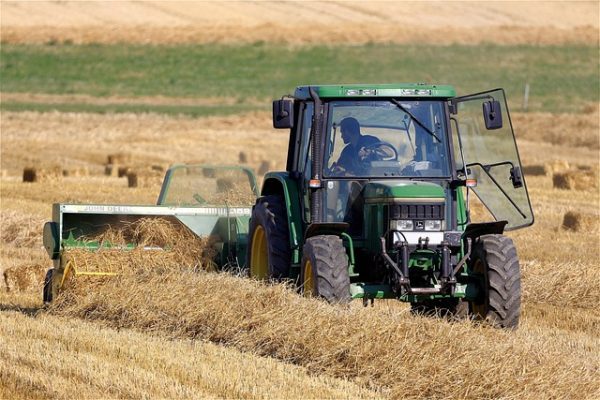 John Deere tractor pulling hay baler during harvest on a farm field.