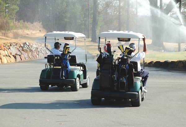 golf-cart-enthusiasts-on-the-course Two golf carts driving on a sunny course with golfers and equipment – representing the community of golf cart owners and enthusiasts featured on Mr. Motor Problems.
