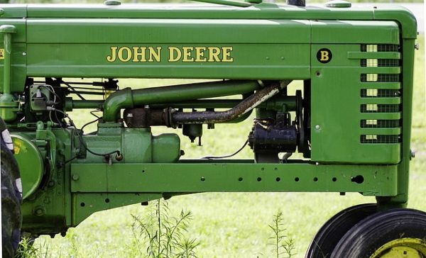 vintage-john-deere-tractor-in-green-field Classic green John Deere tractor side view parked on grass with visible engine details