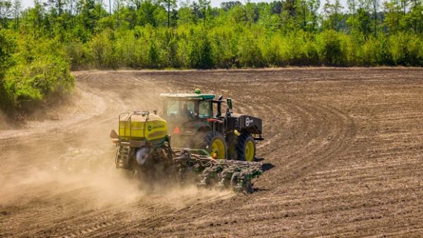 A tractor tills a vast field in rural North Carolina, surrounded by dense greenery.